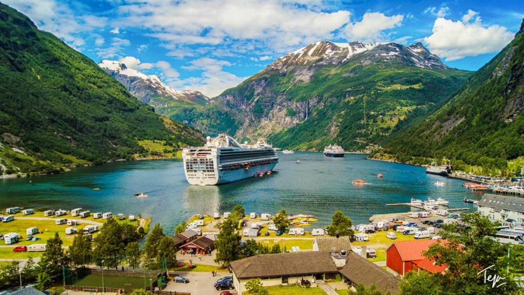 a cruise ship in a body of water surrounded by mountains with Geirangerfjord in the background