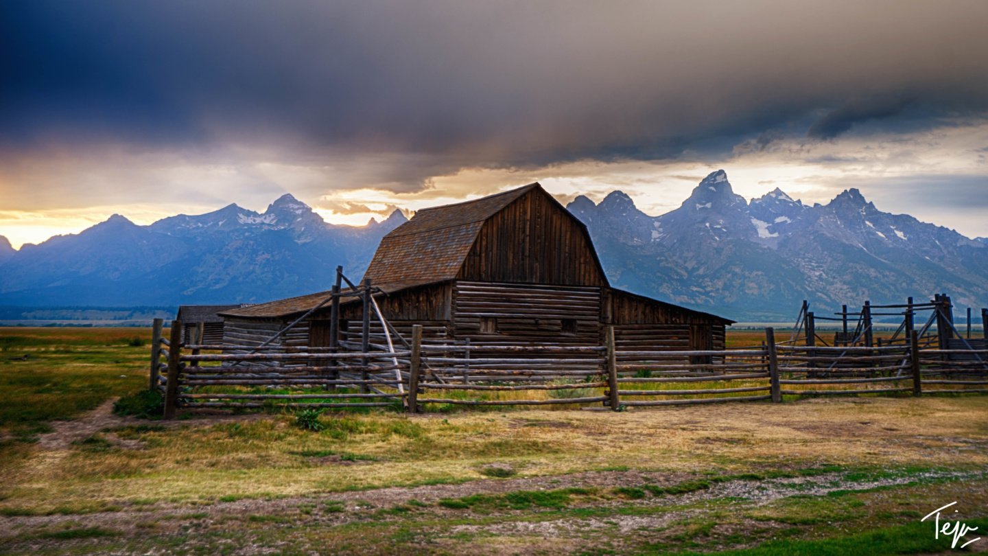 a barn in a field with mountains in the background
