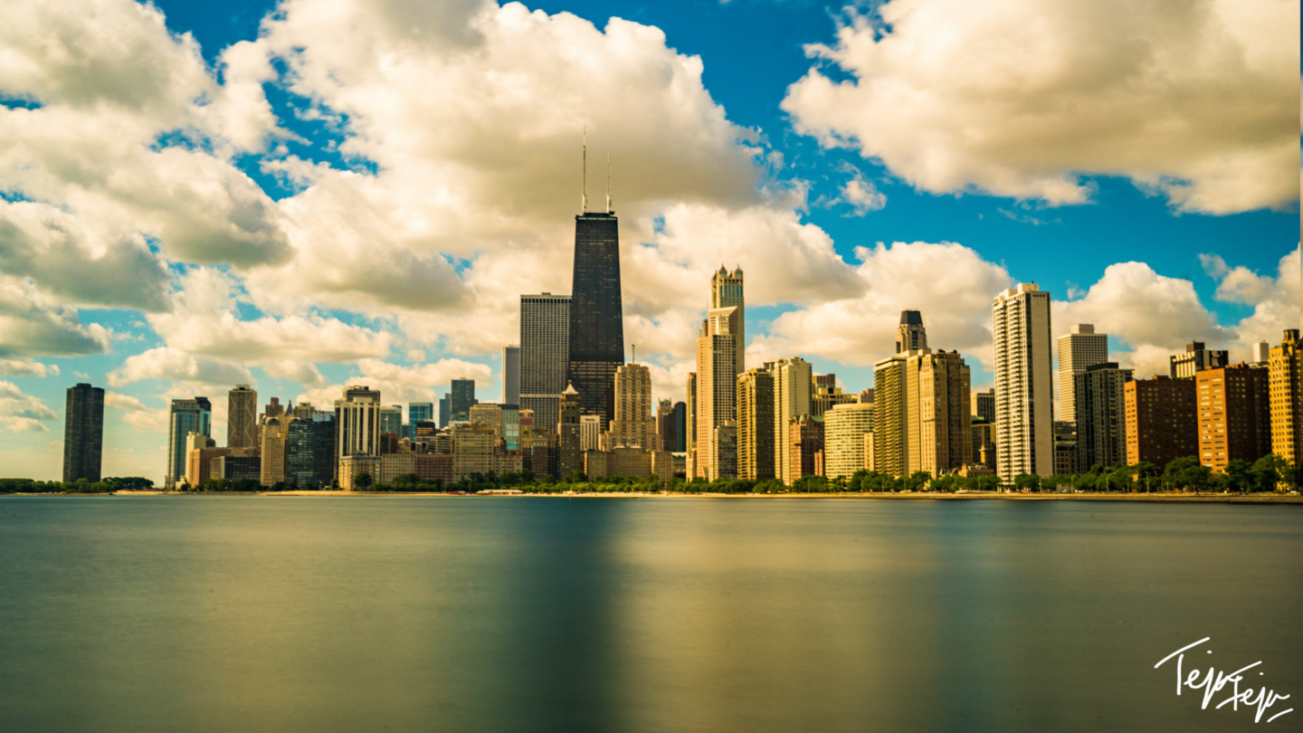 a city skyline with a body of water and clouds in the sky