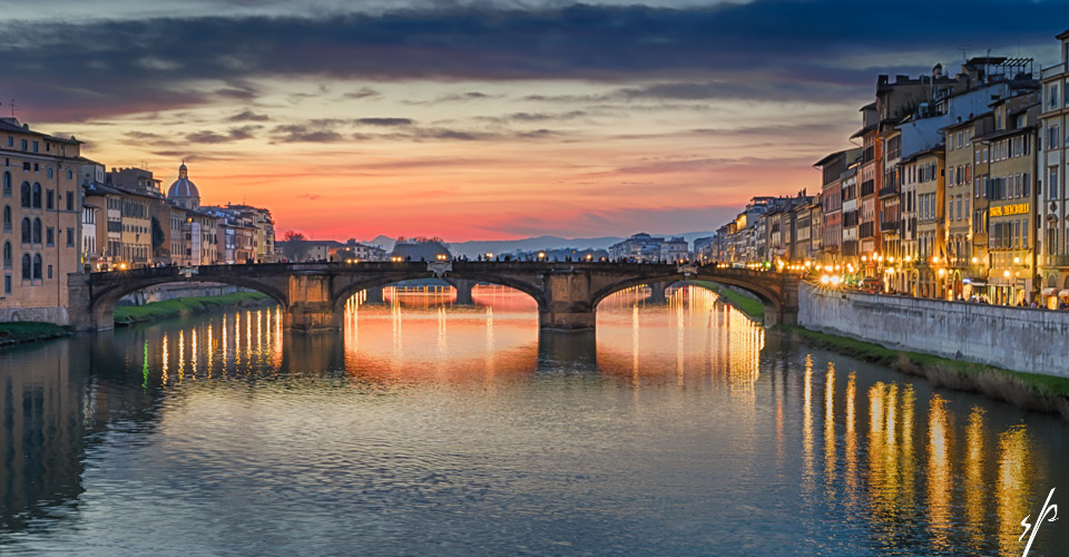 a bridge over a river with buildings and a sunset