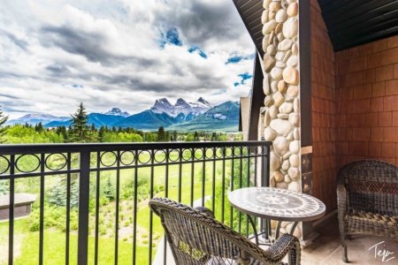 a chair and table on a balcony with a fence and mountains in the background