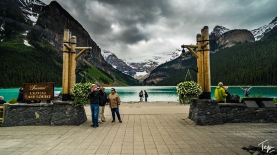 people standing on a walkway with a lake and mountains in the background