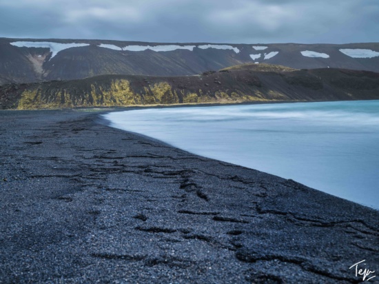 a black sand beach with snow capped mountains in the background