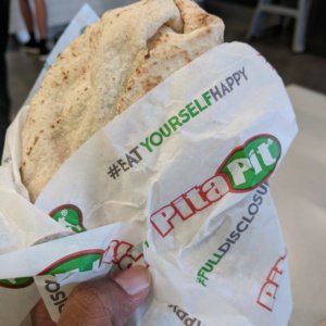 a hand holding a wrapper with a pita in it