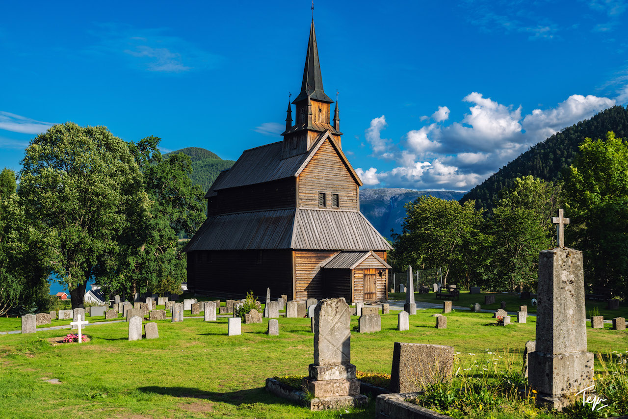 a wooden church with a steeple in a cemetery with Urnes Stave Church in the background