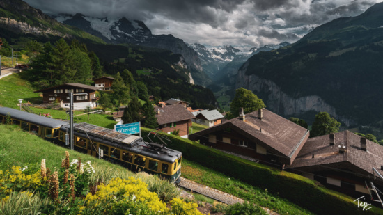 a train going down a hill with houses and mountains in the background