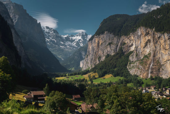 a valley with mountains and houses with Staubbach Falls in the background