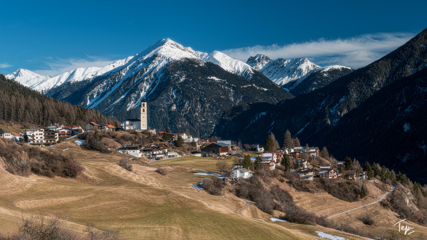 a small town on a hill with mountains in the background