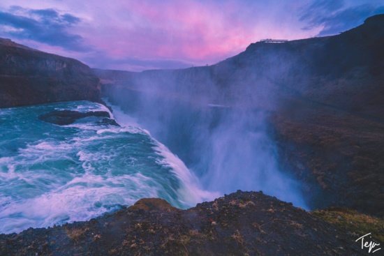 a waterfall with a purple sky