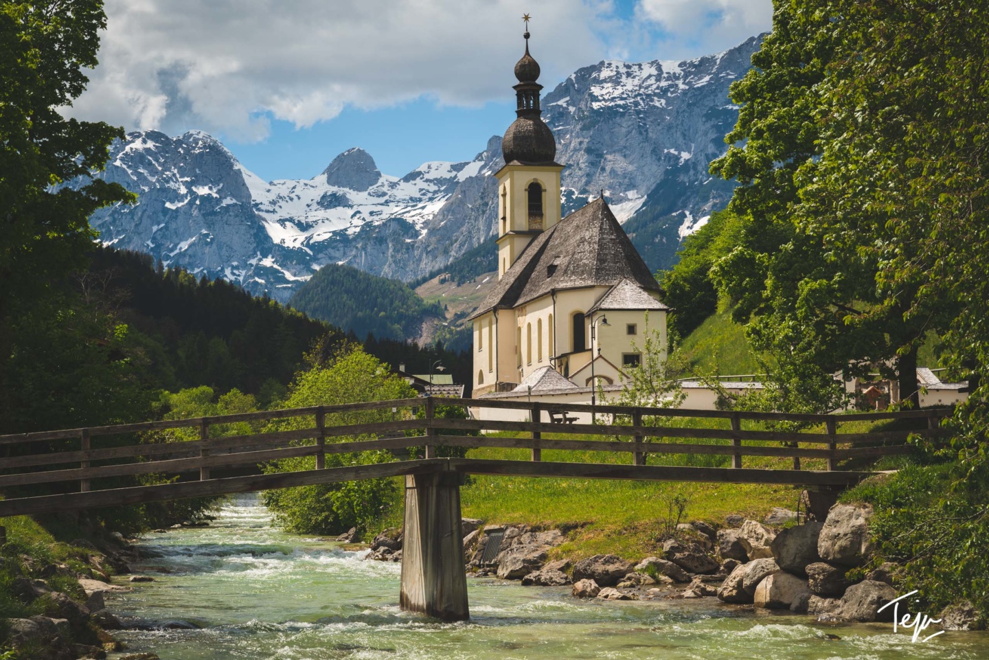 a bridge over a river with a building and mountains in the background
