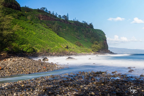a rocky beach with a green hill and blue sky