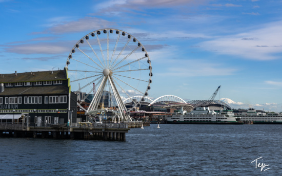 a ferris wheel next to a body of water with Seattle Great Wheel in the background