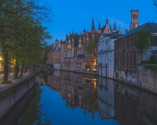 a water way with buildings and trees with Bruges in the background